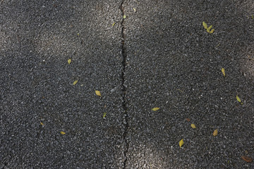 Top view of a slender crack in the middle of black asphalt texture