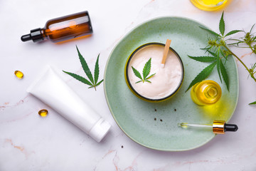 Cosmetics with cannabis oil on a turquoise plate on a light marble background. Copy space, mockup.