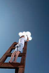 A little boy on the stairs leading to the sky is trying to hang up white cloud