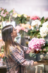 A young girl in a plaid shirt chooses and creates a composition of flowers in a flower shop