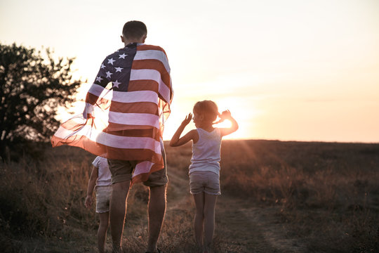 A Happy Family With An American Flag At Sunset.