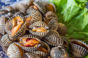 Steamed blanched cockles with Thai seafood dipping sauce and lettuce in the white dish.