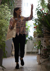 A girl in a plaid shirt with eco bag comes into the store and greets the sellers