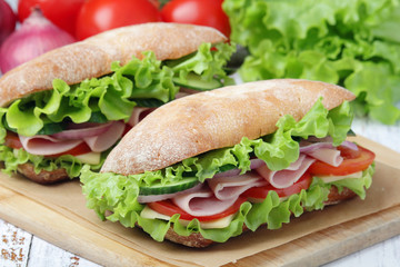 Two sandwiches with fresh vegetables, ham and cheese in ciabatta bread