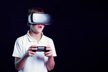 Excited kid in white t-shirt and virtual reality headset standing bending forward playing with...