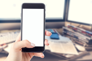 Hand holding a smartphone with a blank screen. Newspapers blurred in the background. Concept of the morning press and telephone in hands.