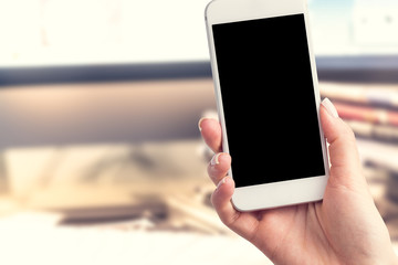 Hand holding a smartphone with a blank screen. Newspapers blurred in the background. Concept of the morning press and telephone in hands.