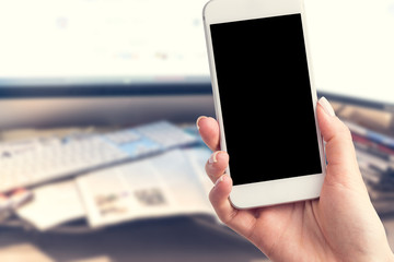 Hand holding a smartphone with a blank screen. Newspapers blurred in the background. Concept of the morning press and telephone in hands.