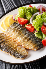 Grilled mackerel fillet with fresh salad and lemon close-up on a plate. vertical
