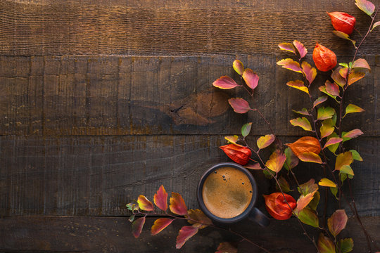 Dark brown clay cup with black coffee and branches of autumn leaves (Spiraea Vanhouttei) with Physalis on the old wooden table. Top view.