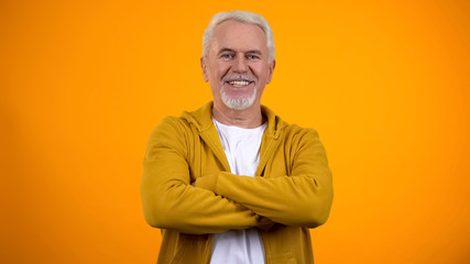 Self-confident senior man with folded arms smiling into camera healthy pensioner