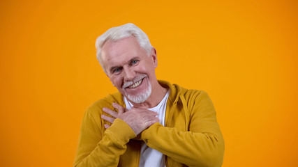 Kind old person crossing palms on breast, smiling to camera, sincerity concept