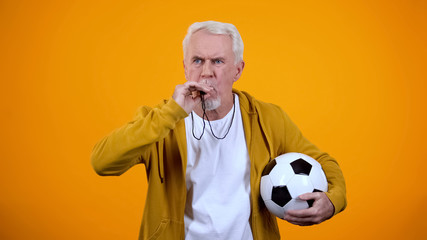 Dissatisfied elderly football trainer blowing whistle during sport competition