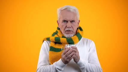 Sick elderly man in scarf holding cup with hot tea, treating cold illness, ad