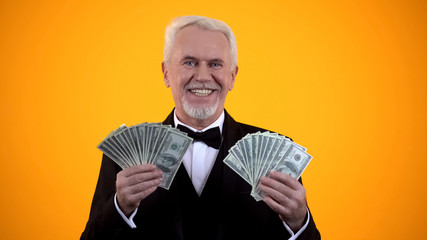 Wealthy elderly man in suit holding dollars and smiling, successful business