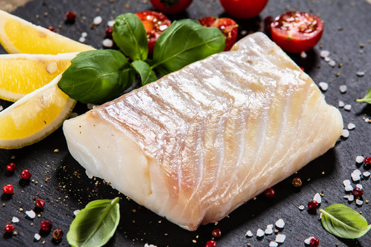 Fresh raw cod with herbs served on black stone on wooden table