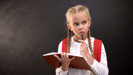 Thoughtful schoolgirl with pen and copybook thinking about complicated task