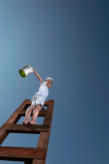 Cute little boy is trying to paint the sky with tassel , climbing up the stairs to very high