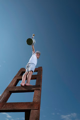 Cute little boy is trying to paint the sky with tassel , climbing up the stairs to very high