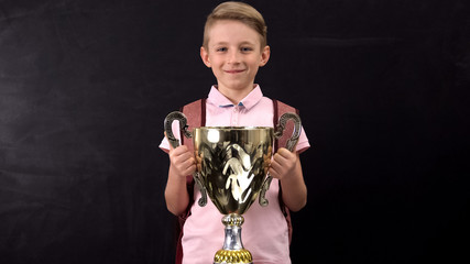 Happy schoolboy holding bowl award, winning sports tournament, successful child