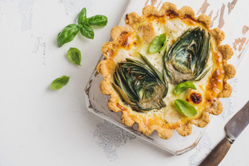 Homemade quiche tart with with artichoke on light wooden background. Vintage style. Top view.