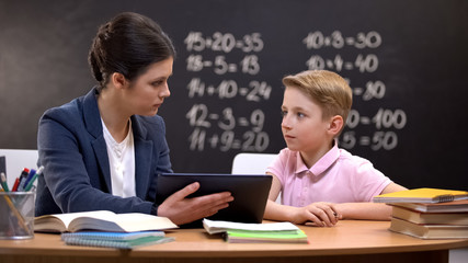 Female teacher explaining schoolboy homework on tab, private lesson, innovations