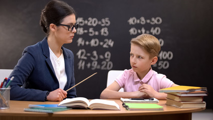 Scared schoolboy cautiously looking at strict teacher with pointer, education