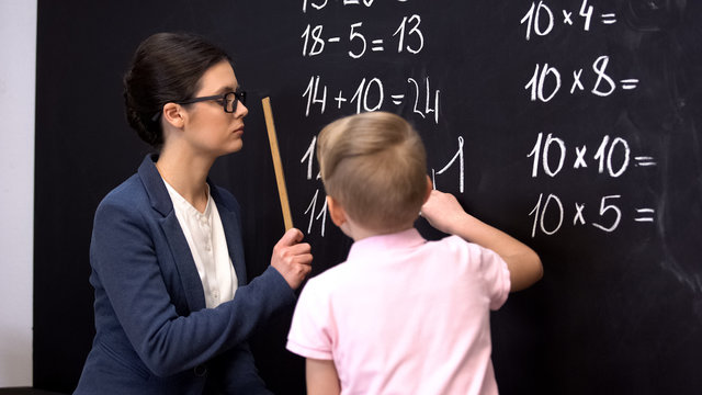 Teacher hitting schoolboy with ruler, boy writing on blackboard, punishment