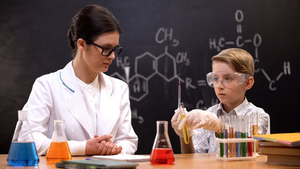 Chemistry teacher watching schoolboy taking liquid into pipette, private lesson