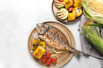 From above grilled fish with lemon served with different vegetables on dishes over white background