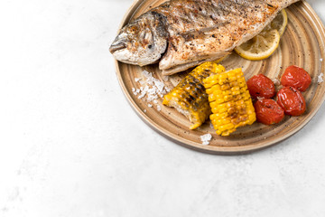 From above grilled fish with lemon served with different vegetables on dishes over white background
