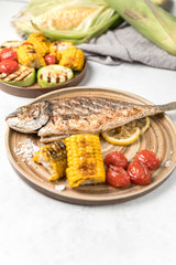 From above grilled fish with lemon served with different vegetables on dishes over white background