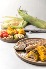 From above grilled fish with lemon served with different vegetables on dishes over white background