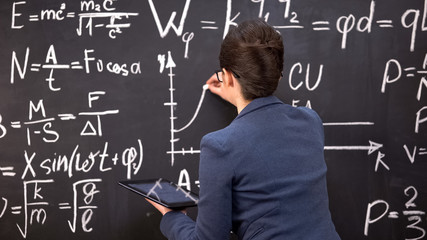 Female teacher drawing graph on chalkboard and holding tablet, innovations