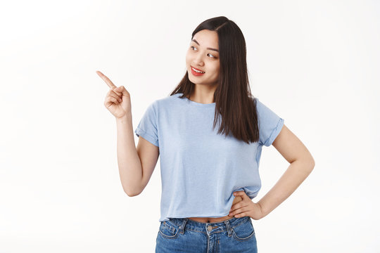 Curious happy friendly-looking pretty asian girl acne prone skin look away intrigued pointing gazing left interested picking making choice cool store asking merchant question hold hand waist