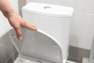 Unrecognizable man closes the toilet lid. White bathroom interior