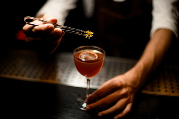 Professional bartender serving a cocktail in the glass with a caramelized lemon slice adding a yellow flower