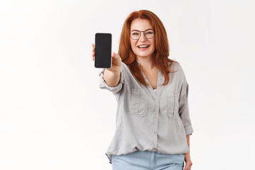 Naklejka premium Woman sharing useful app. Charming elegant redhead middle-aged businesswoman mom wear glasses extend arm hold smartphone show phone screen display promote application white background