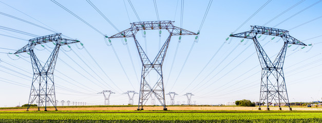 Panoramic view of a row of electricity pylons in the countryside with dozens of other pylons in the...