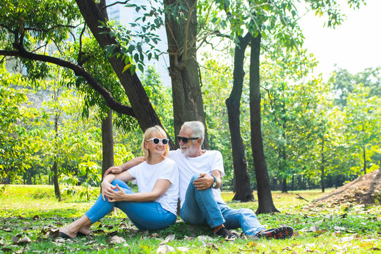 Happy Senior Caucasian Couple Relax Hugging, Smiling And Laughing They Are Sitting Together In The Park And Dressed Up  Jeans And White T-shirt. They Have Good Relationship In Marriage Life.