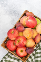 Fruit in a wooden box on a light gray background. Apples, pears, peaches and plums