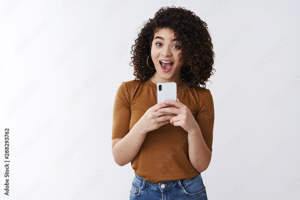 Wall mural Say cheese. Cheerful attractive amused happy curly-haired girlfriend holding smartphone taking picte friend asking smile make selfie mirror excited standing white background upbeat