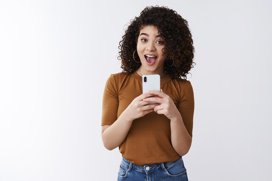 Say cheese. Cheerful attractive amused happy curly-haired girlfriend holding smartphone taking picte friend asking smile make selfie mirror excited standing white background upbeat