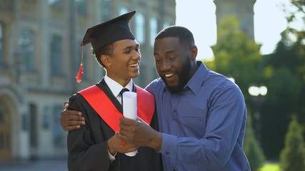 Dad feeling proud of teenage son holding university diploma, graduation success