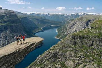 Three tourists on Trolltunga rock, mountain lake landscape, Norway