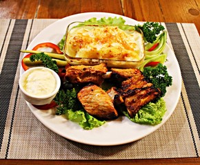 Grilled pork slices, potatoes in a glass bowl and assorted fresh vegetables salad
