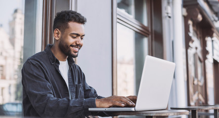 Smiling man student using laptop computer in a city. Young handsome men having coffee break. Modern lifestyle, connection, business, freelance work concept