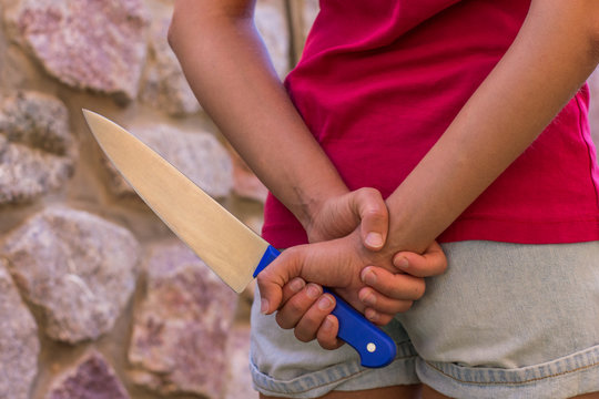 child female violence concept picture of steel kitchen knife in young girl hand behind back 