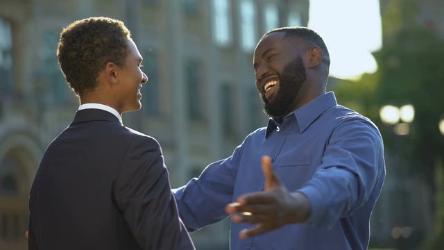 Excited african man feeling proud of young son in prom suit, college graduation