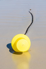 Close-up view of a large yellow buoy and its anchorage chain, used as a launching channel marker, lying on the wet sand on the beach in Penvenan, Brittany, France, under a bright sunshine.